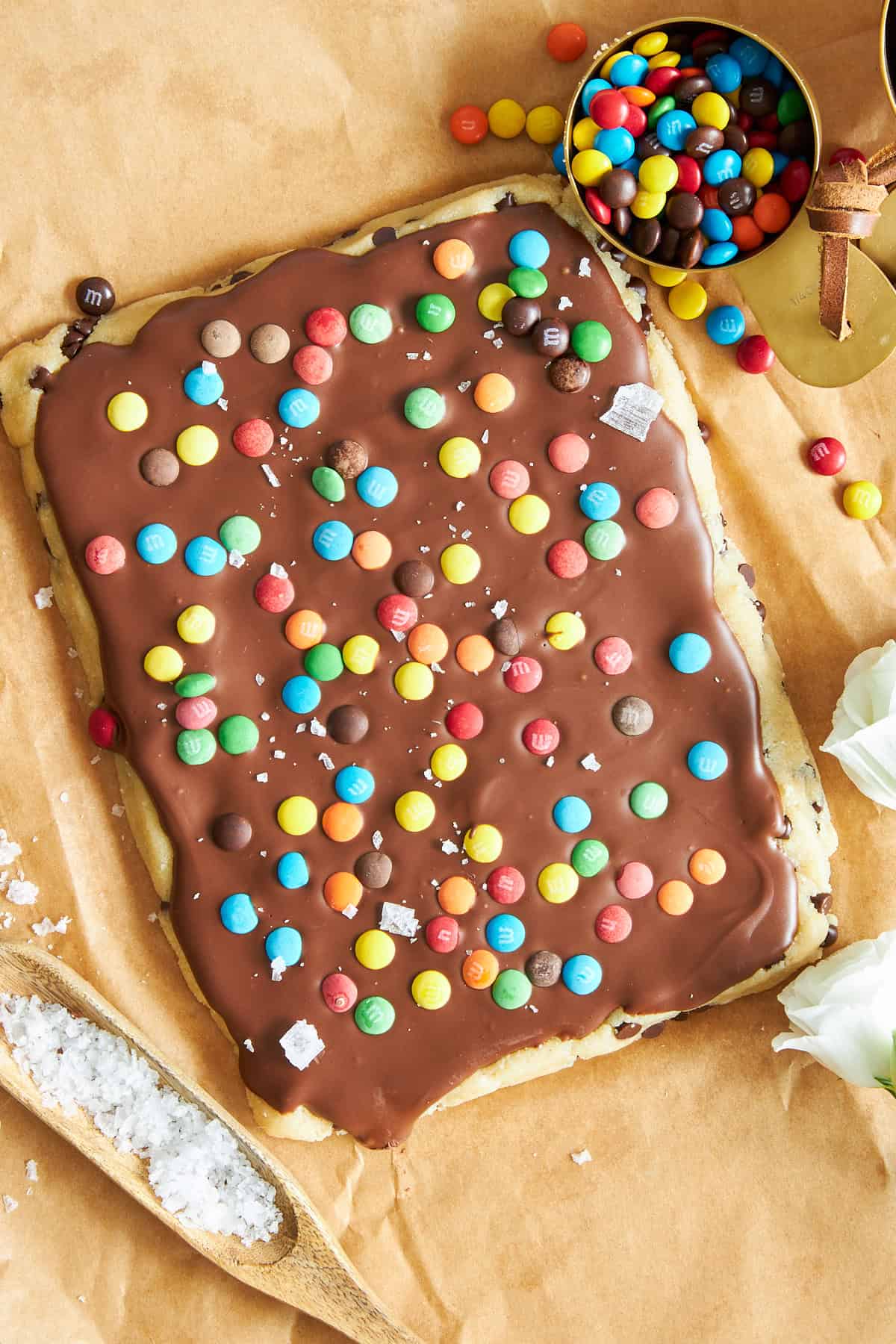 A slab of cookie dough bark topped with melted chocolate and mini M&Ms.