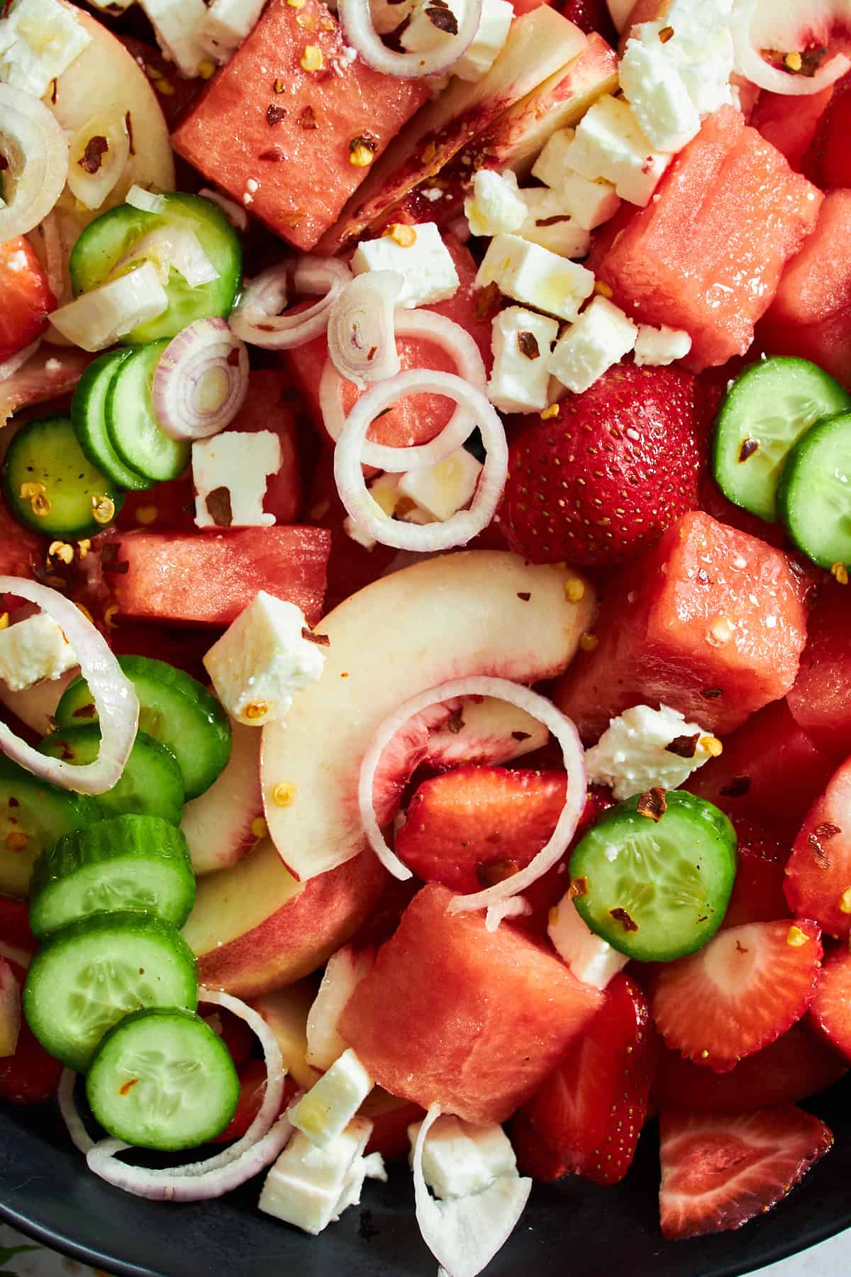 Close up image of watermelon cucumber salad with strawberries, peaches, and feta. 