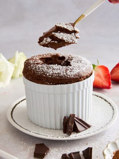 A spoon holding a bite of chocolate soufflé over a ramekin of soufflé.