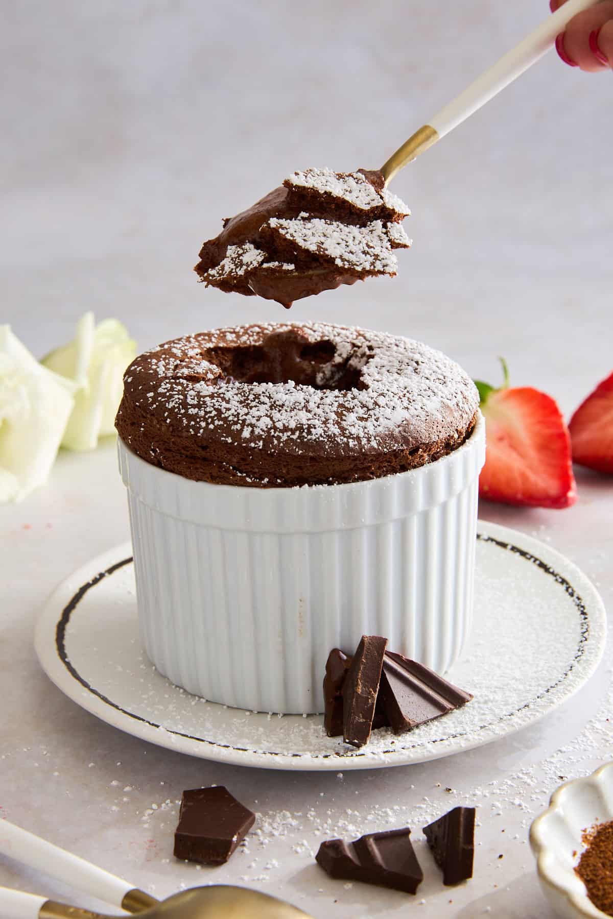 A spoon lifting a bite from a ramekin of chocolate souffle. 