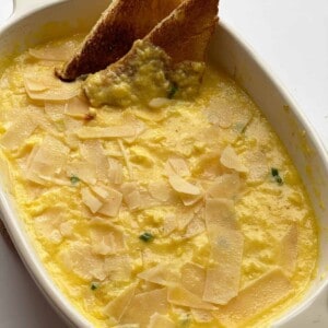 A casserole dish of baked scrambled eggs with two pieces of toasted bread sticking out.