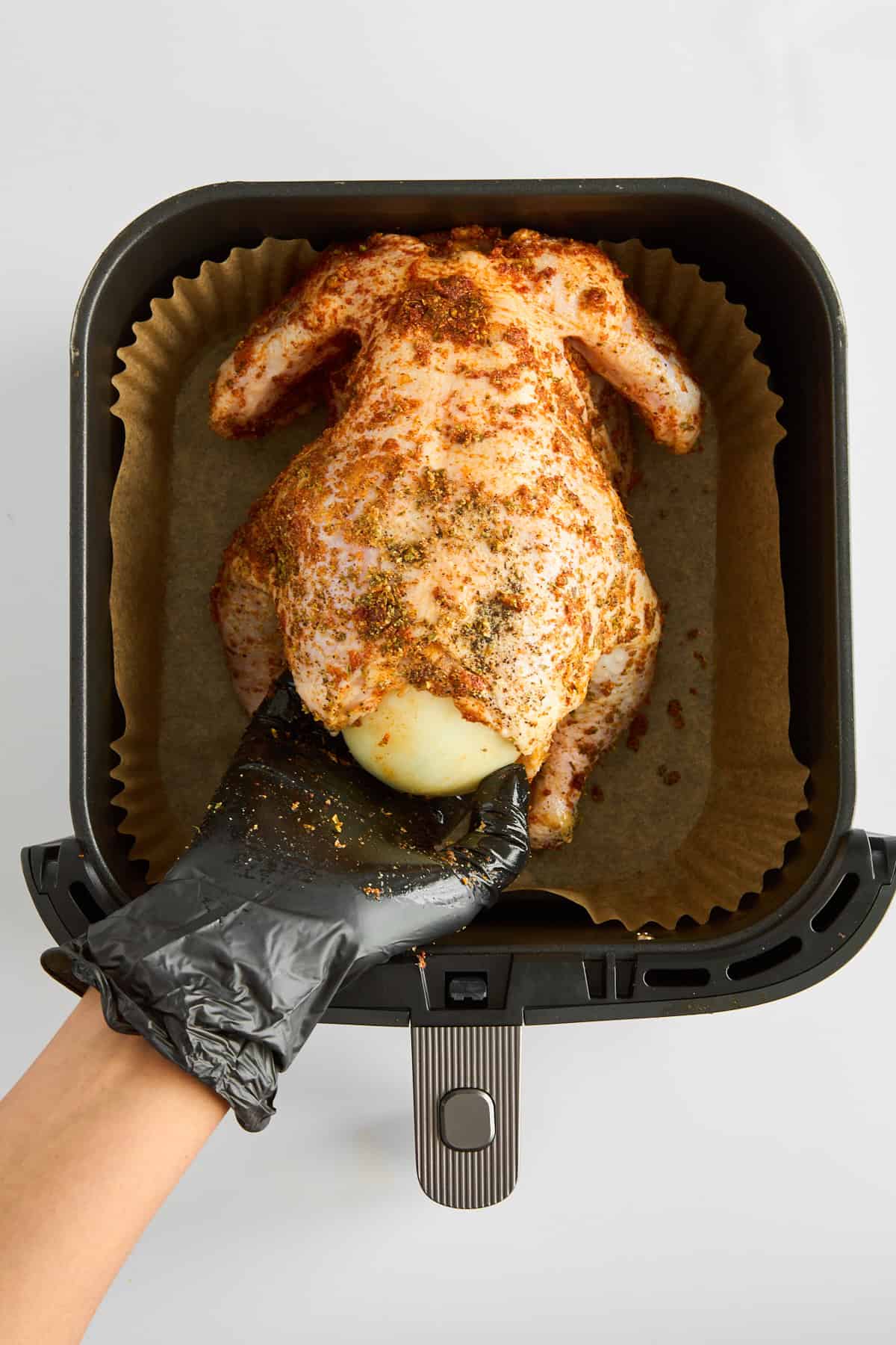 A gloved hand stuffing a raw whole chicken in an air fryer. 