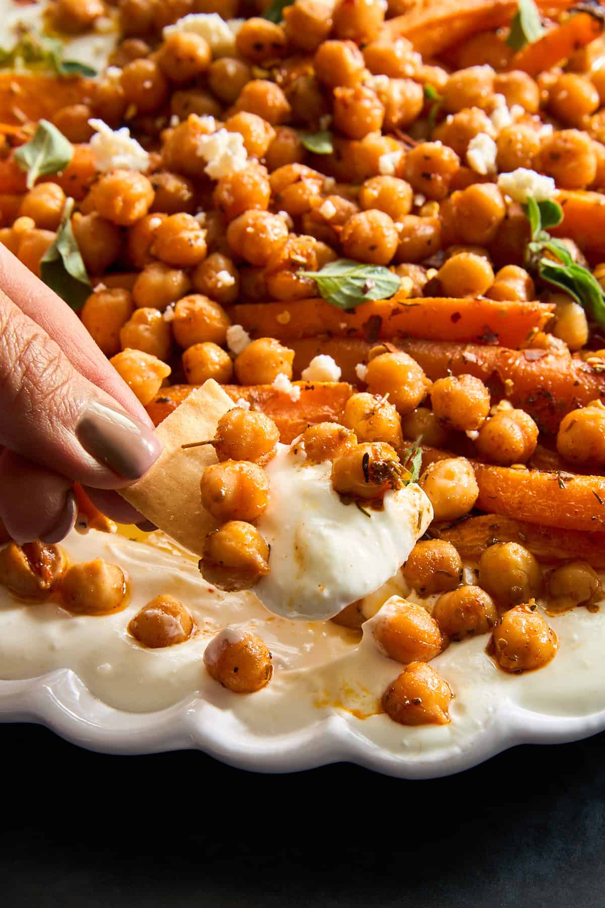 A hand dipping a pita chip into chickpeas and roasted carrot whipped feta. 