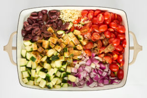 Chopped veggies being seasoned in a baking dish.