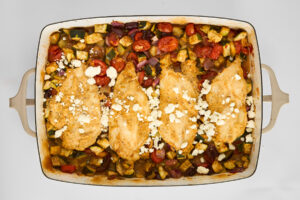 Hummus baked chicken and veggies in a baking dish topped with feta.