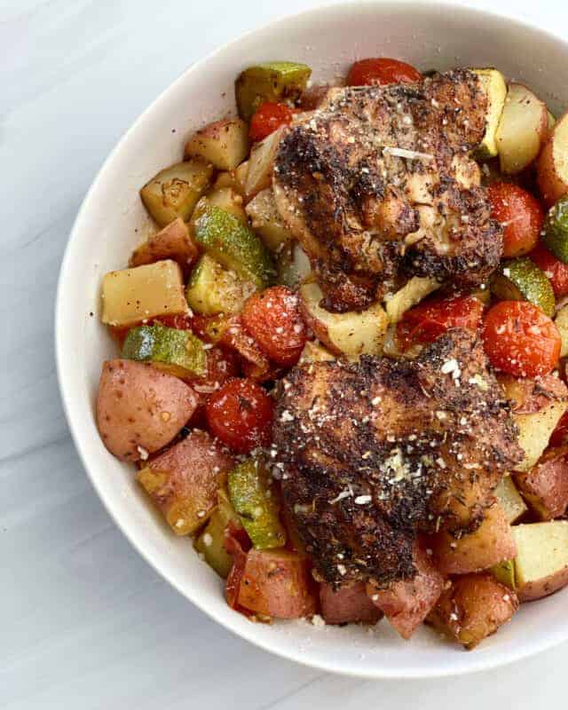 a close up image of a bowl full of cooked seasoned chicken thighs on top of a bed of veggies.