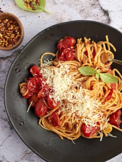 a black plate with a serving of one pan spaghetti with roasted tomatoes topped with Parmesan cheese