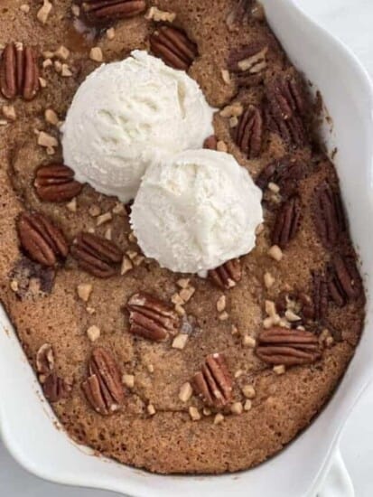 pecan pie cobbler in a white baking dish topped with two scoops of vanilla ice cream