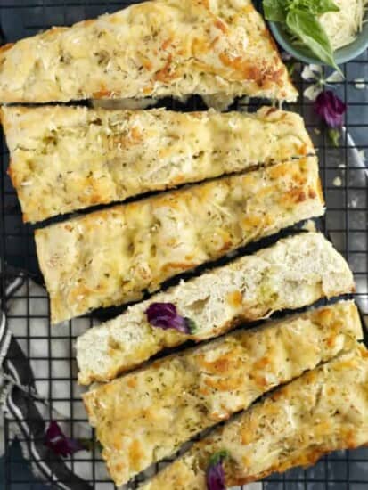 pieces of no knead cheesy focaccia bread on a cutting board with fresh basil.