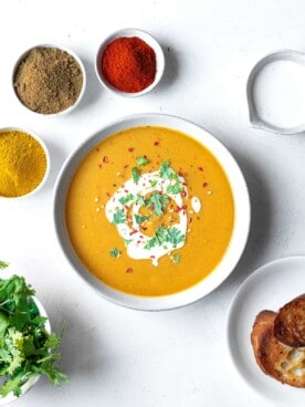 a bowl of Egyptian lentil soup with spices around it