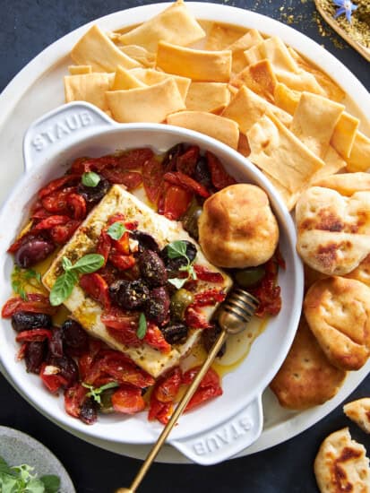 A baking dish of Mediterranean baked feta dip surrounded by pita chips and puffs.