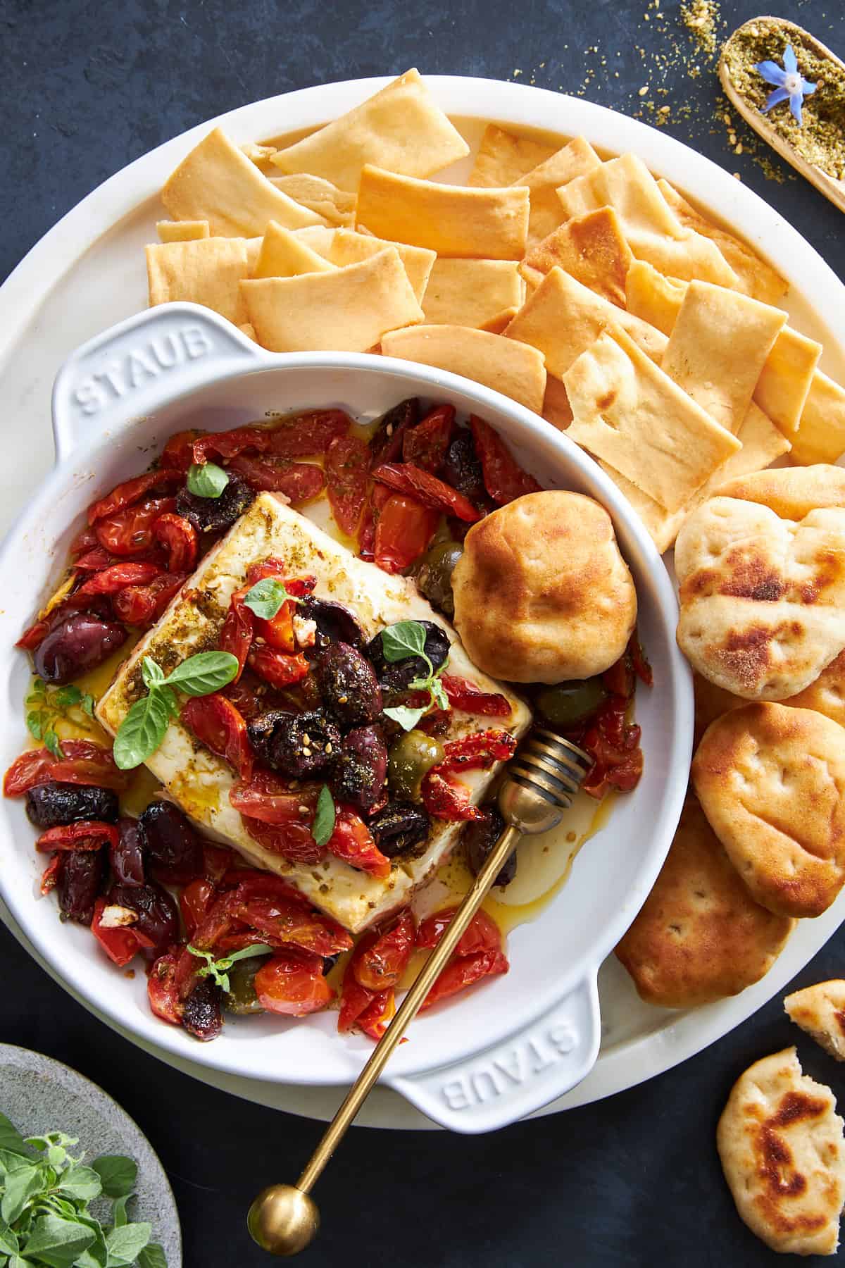 A baking dish of Mediterranean baked feta dip surrounded by pita chips and puffs.