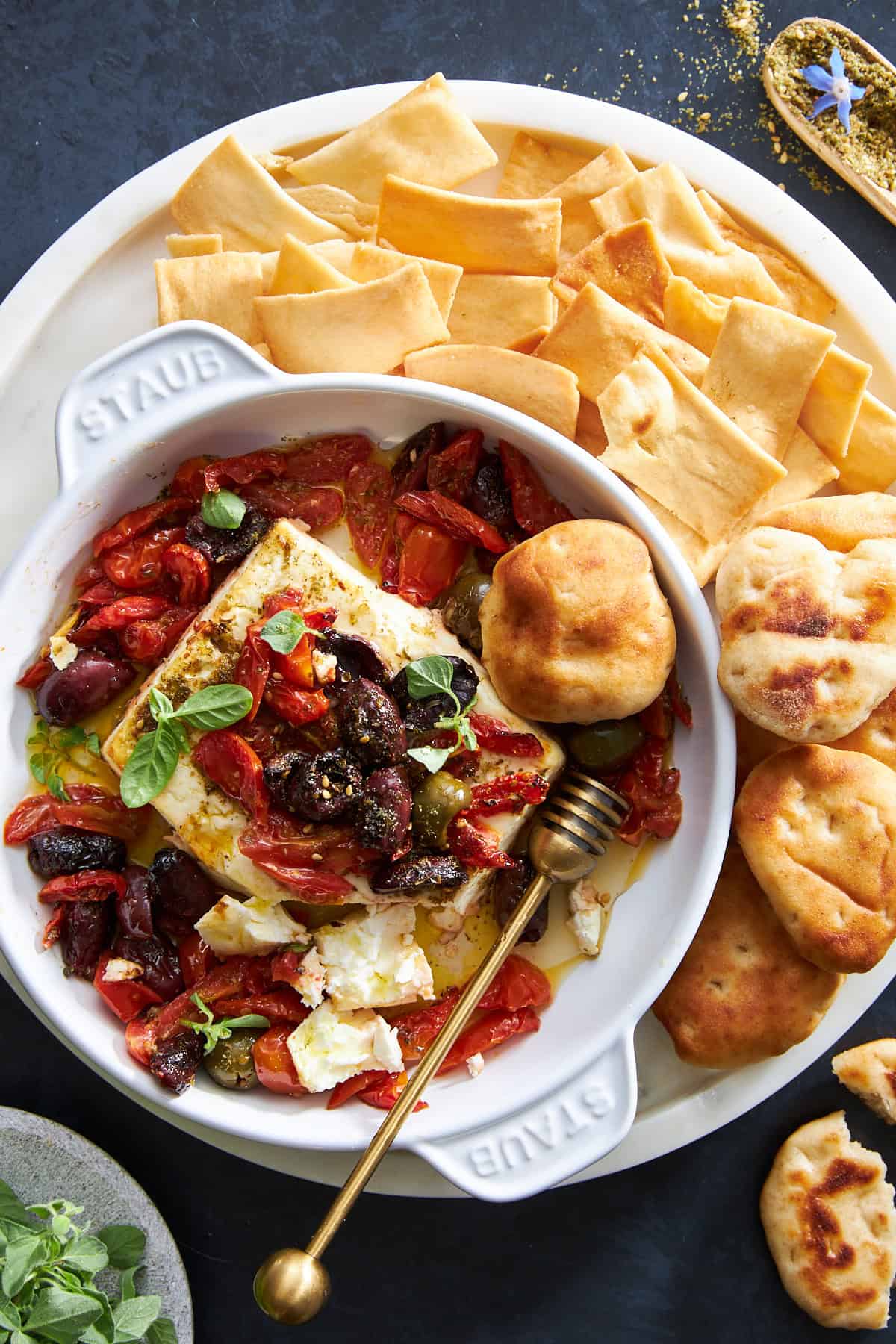 A bowl of baked feta dip surrounded by pita chips and puffs. 