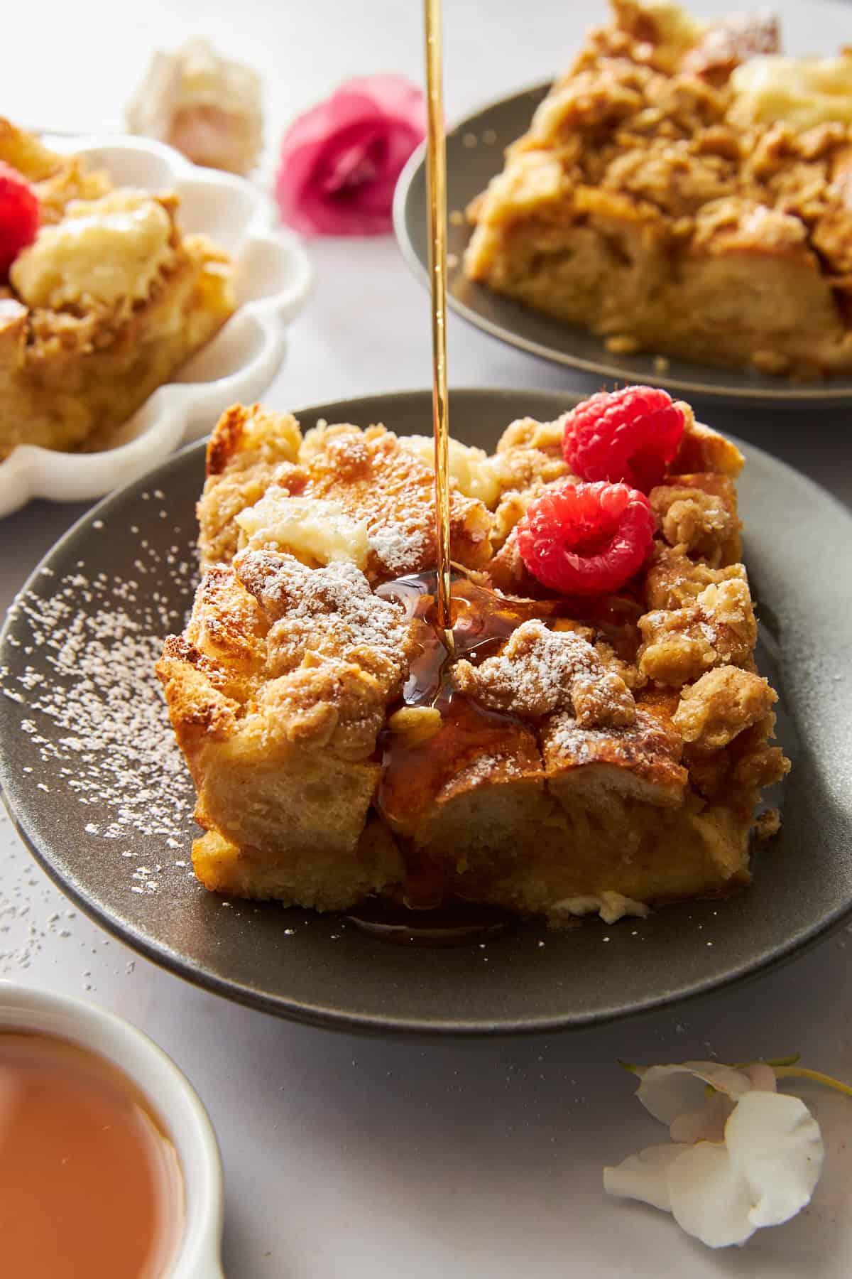 A slice of cream cheese french toast on a plate with maple syrup being drizzled on top. 