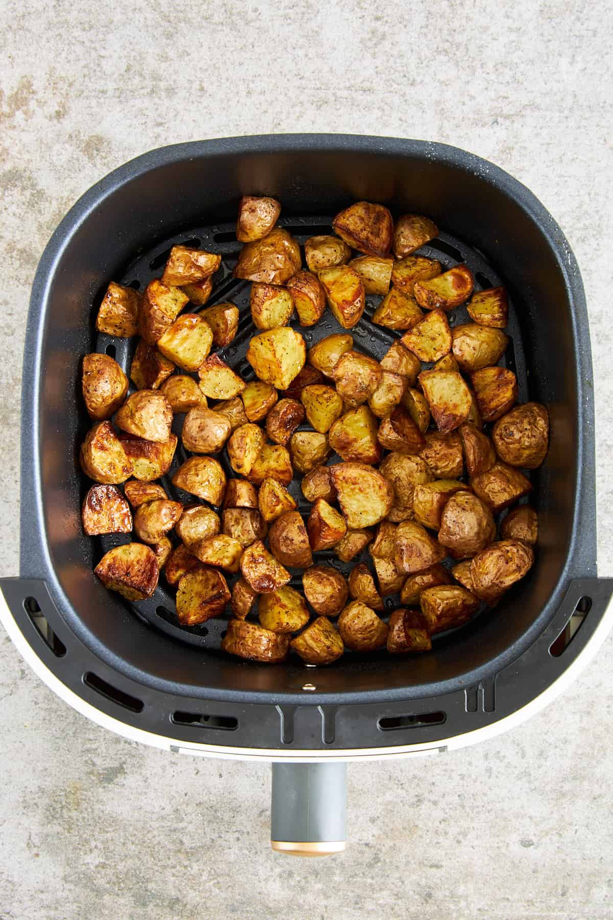 Cooked Greek potatoes in an air fryer basket. 