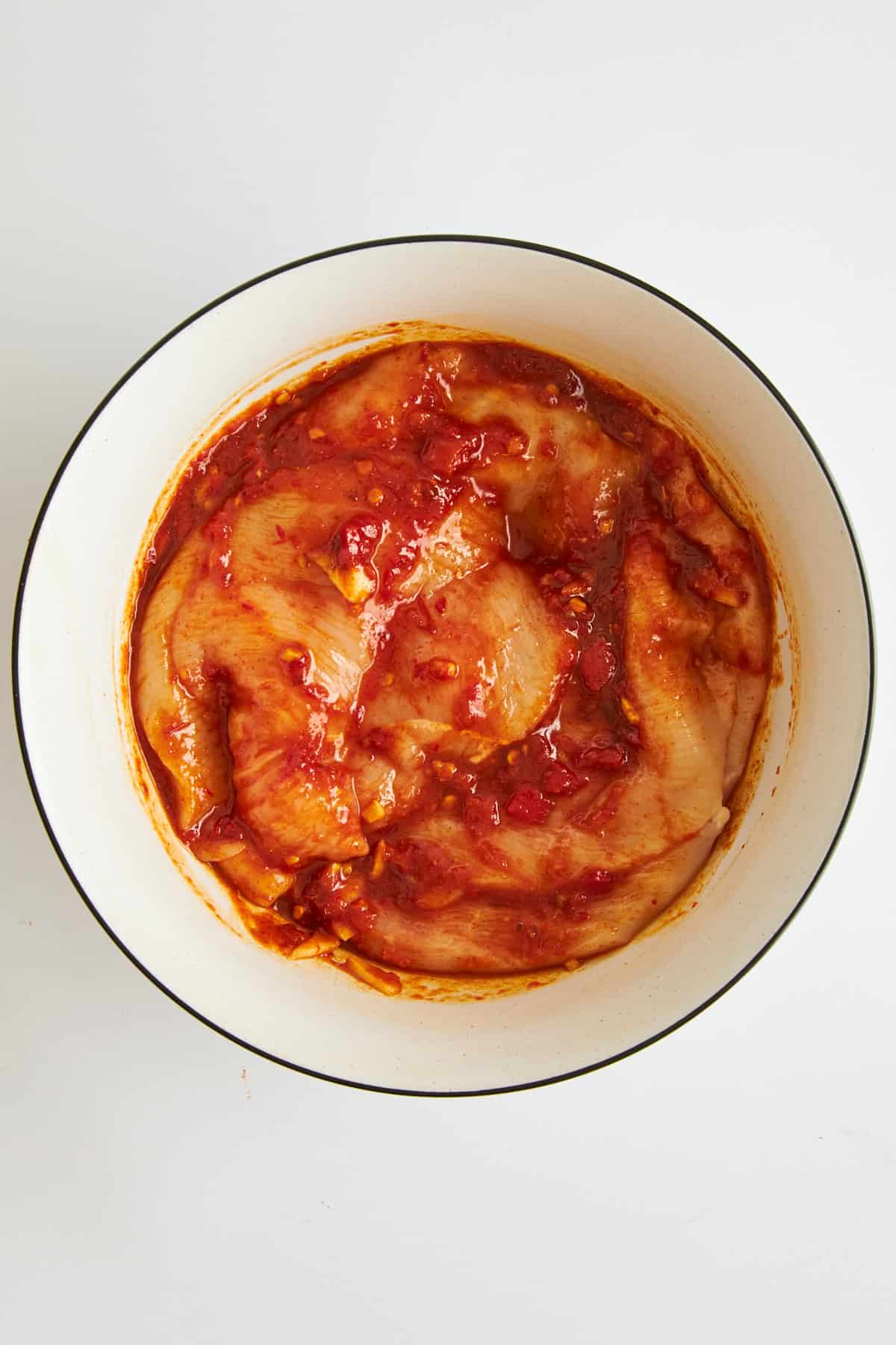 Raw chicken covered in honey harissa marinade in a bowl. 