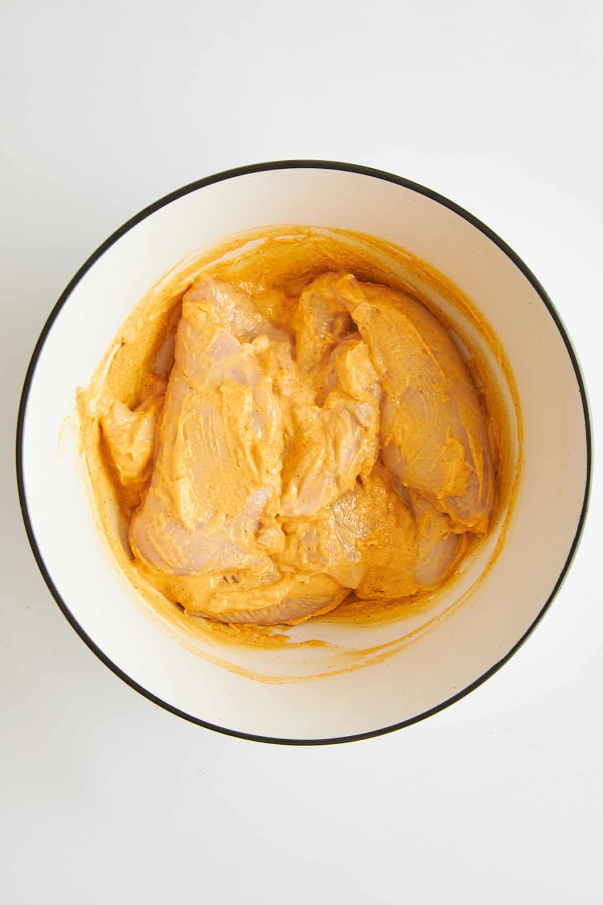 Raw chicken coated in hummus marinade in a bowl. 