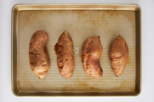 Four sweet potatoes on a baking sheet.