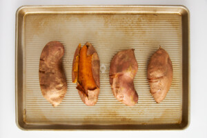 Four roasted sweet potatoes on a baking sheet.