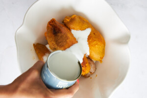 coconut milk being poured over peeled sweet potatoes.