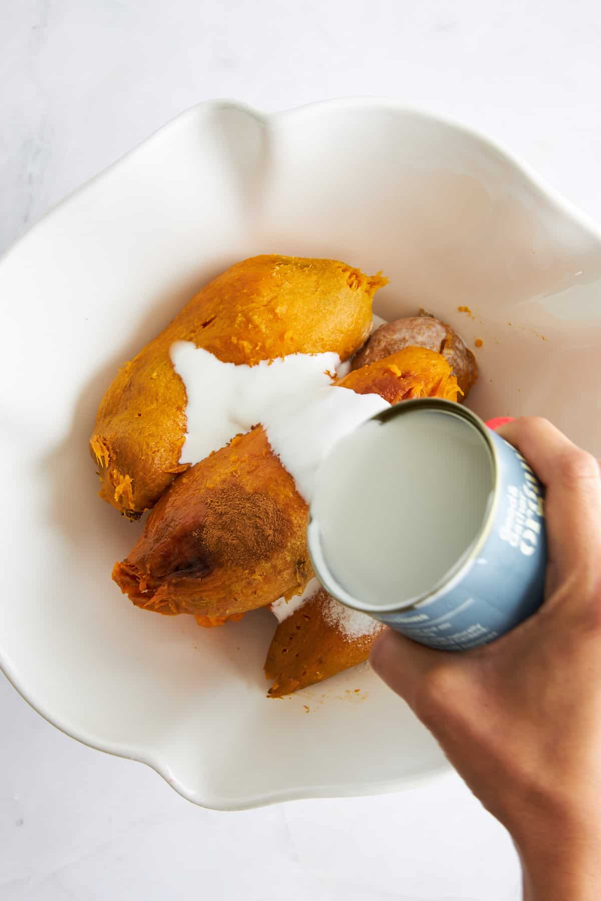 Coconut milk being poured over baked sweet potatoes in a bowl. 