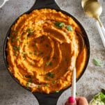 A hand holding a spoon in a bowl of dairy free mashed sweet potatoes.