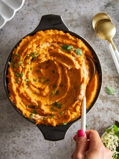 A hand holding a spoon in a bowl of dairy free mashed sweet potatoes.