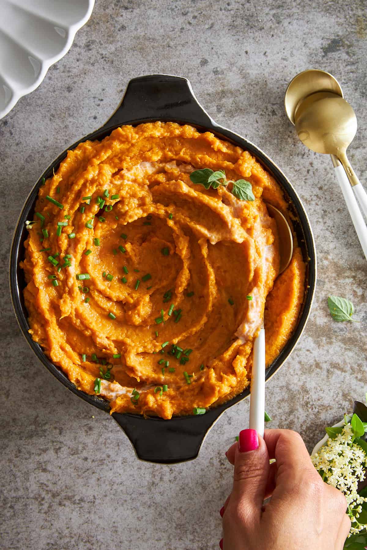 A hand holding a spoon in a bowl of dairy free mashed sweet potatoes.