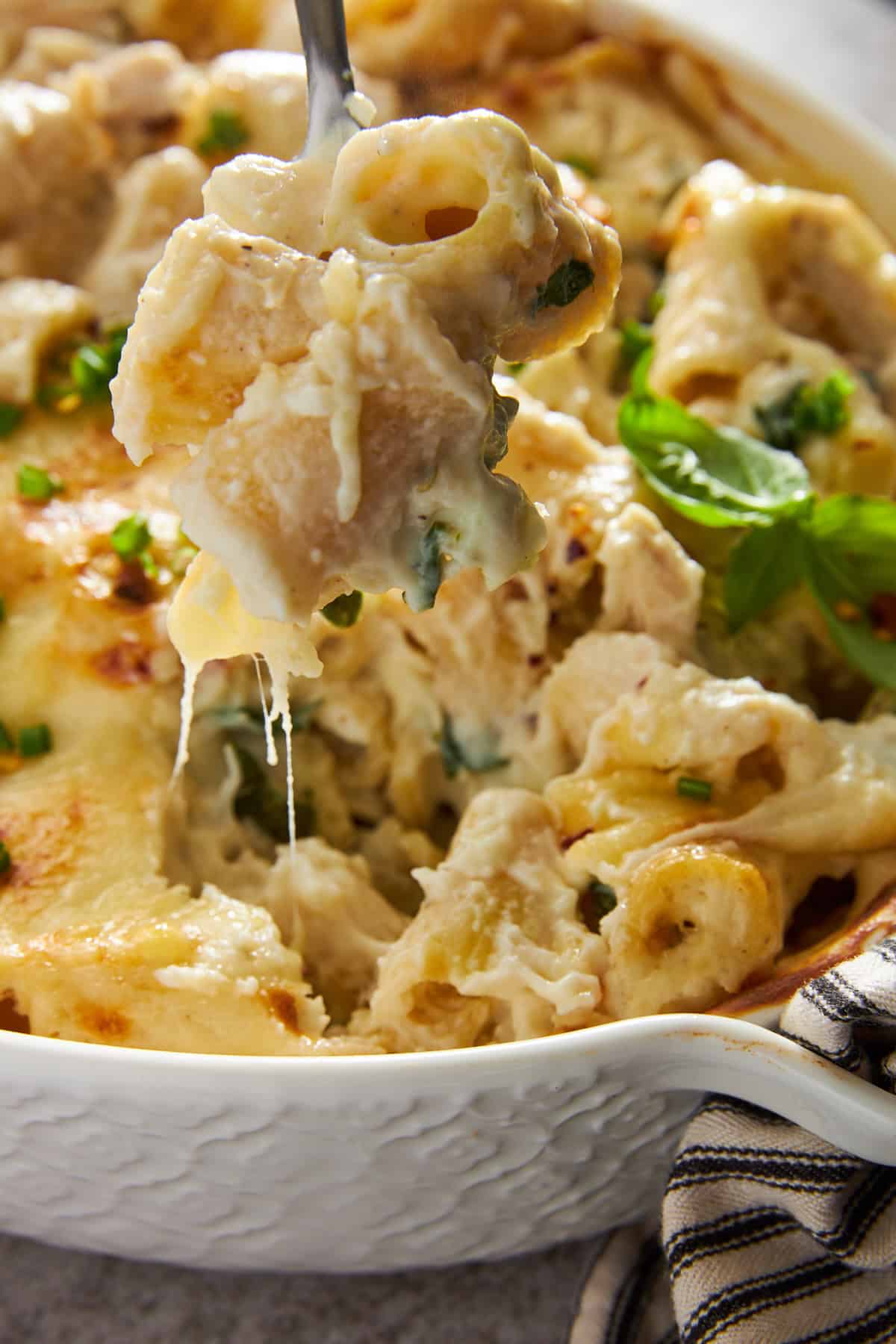 A fork lifting a bite of chicken spinach pasta bake from a baking dish. 