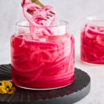 A fork lifting pickled red onions from a jar.