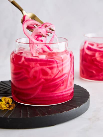 A fork lifting pickled red onions from a jar.