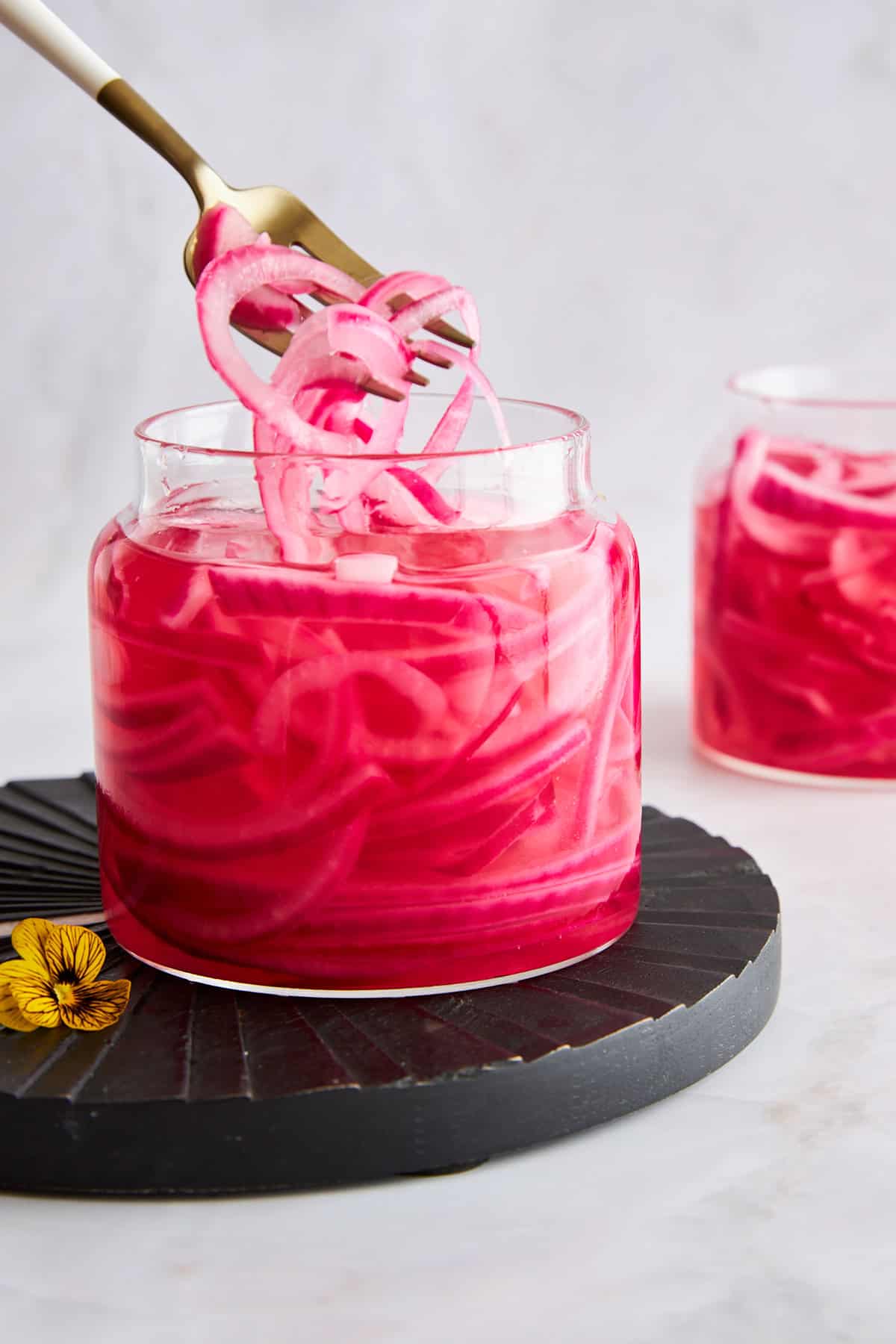 A fork lifting pickled red onions from a jar.