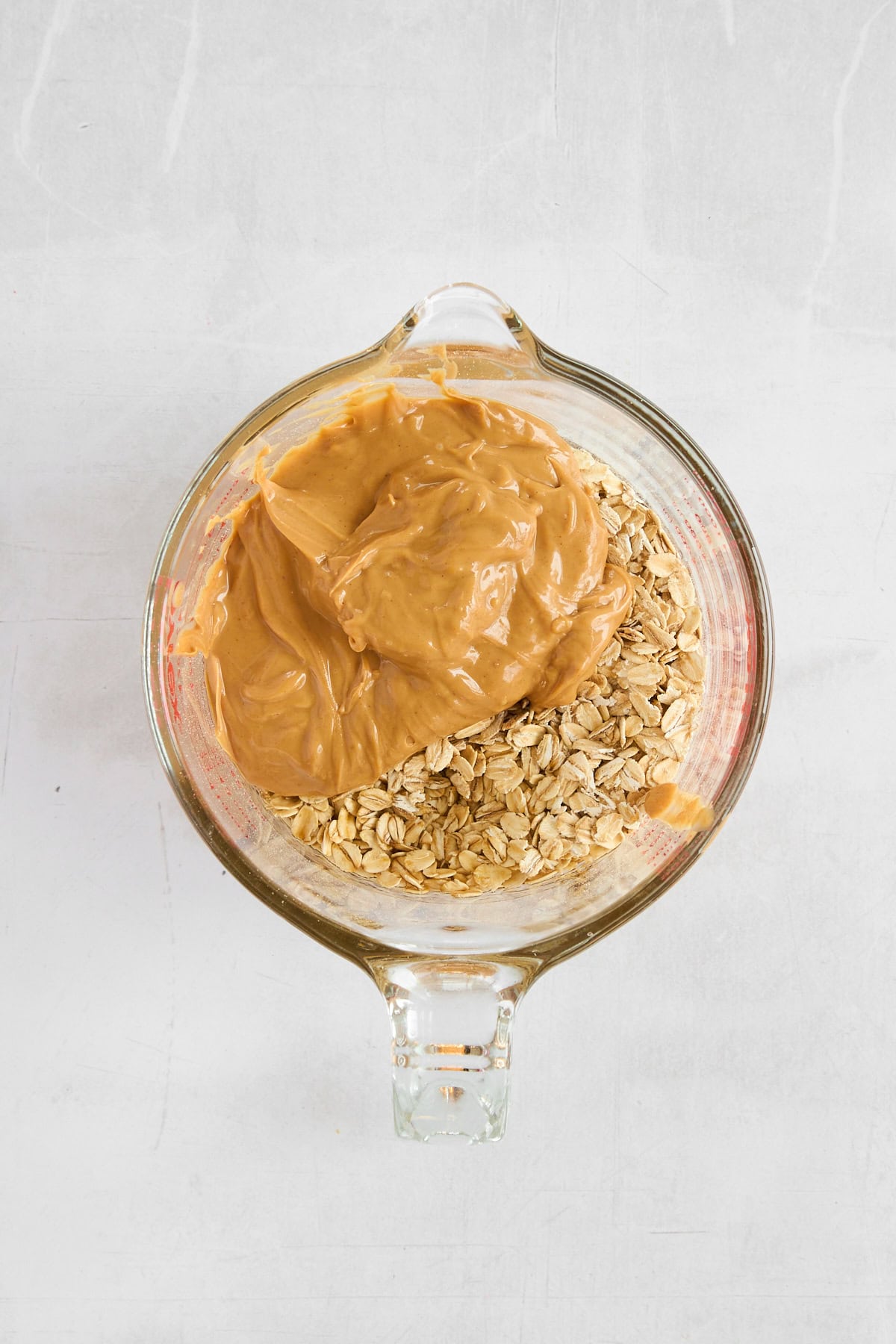 Oats, peanut butter, and maple syrup in a glass measuring cup. 