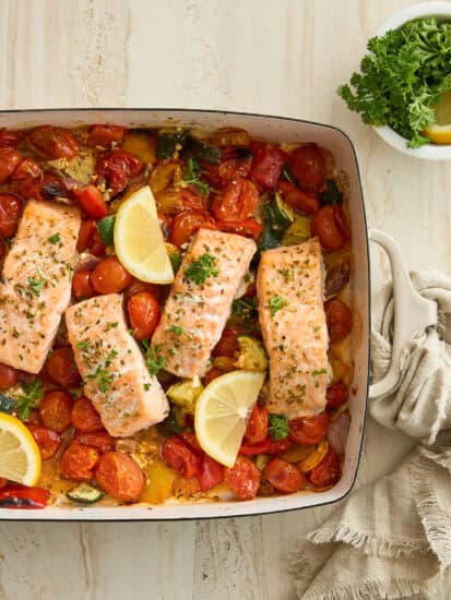 Baked feta salmon in a dish with tomatoes and lemon wedges.