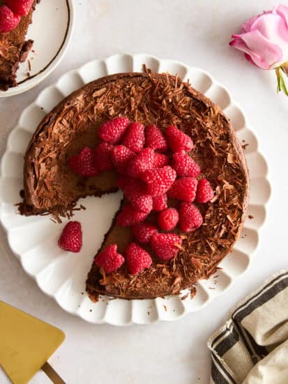 A flourless chocolate cake topped with raspberries with a slice missing.