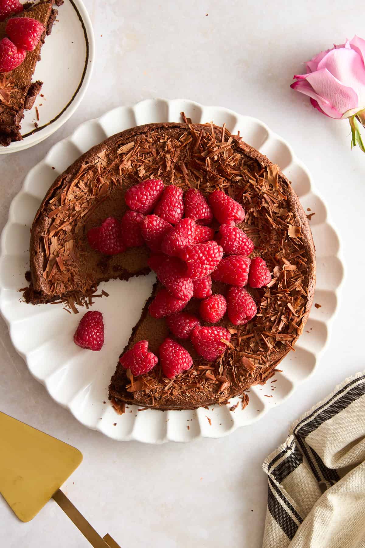 A flourless chocolate cake topped with fresh raspberries with a slice missing. 