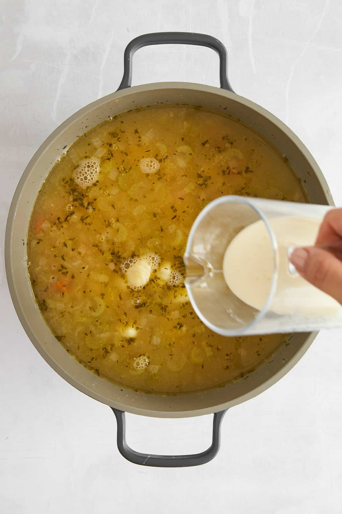 Cream being poured into a pot of chicken and gnocchi soup. 