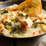 A spoon lifting a scoop of chicken and gnocchi soup from a bowl.