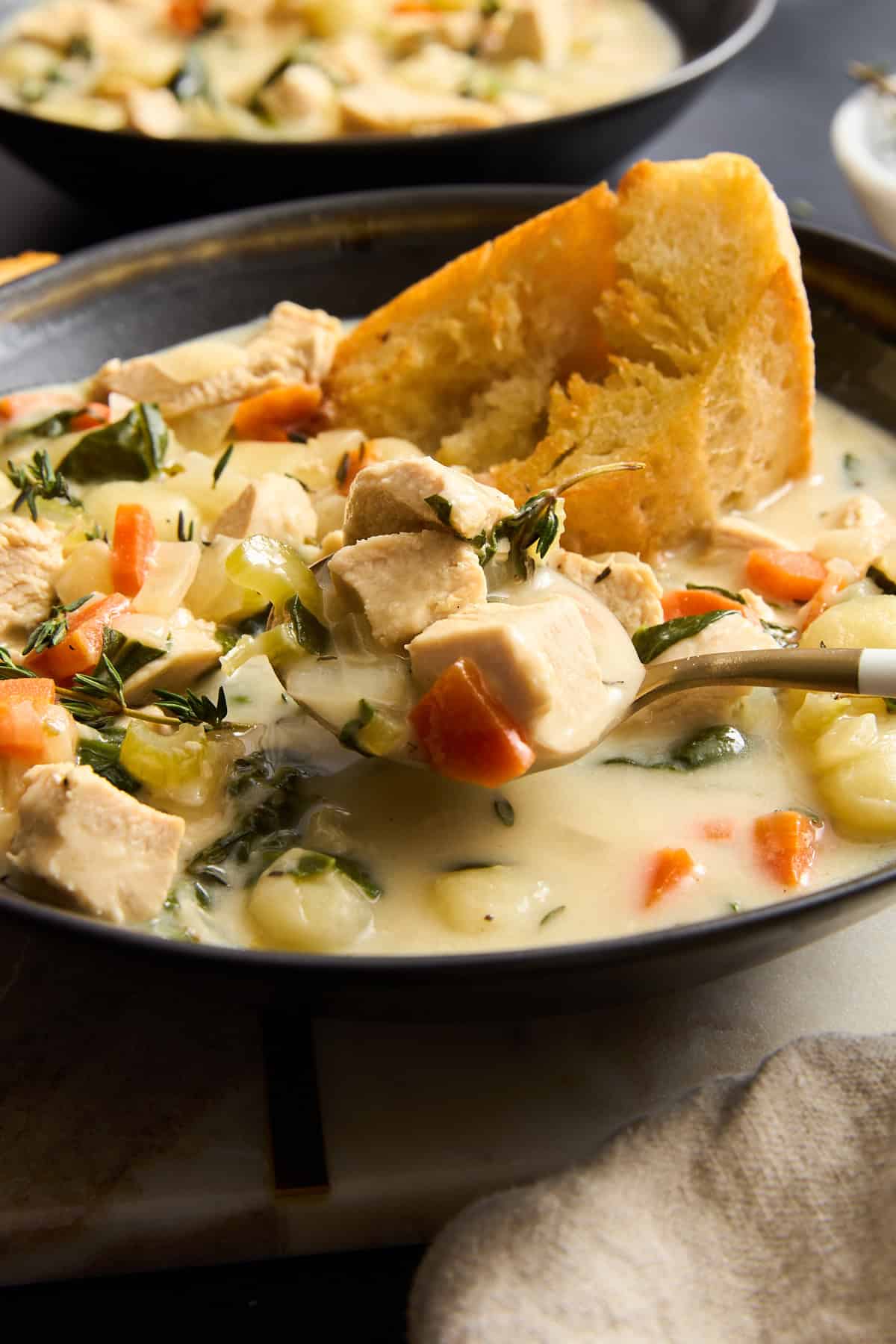 A spoon lifting a scoop of chicken and gnocchi soup from a bowl.