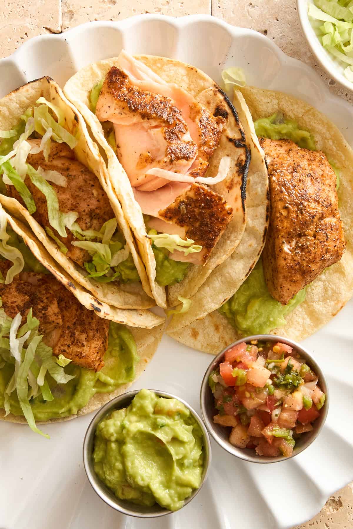 A plate of four salmon tacos with guacamole and pico de gallo. 