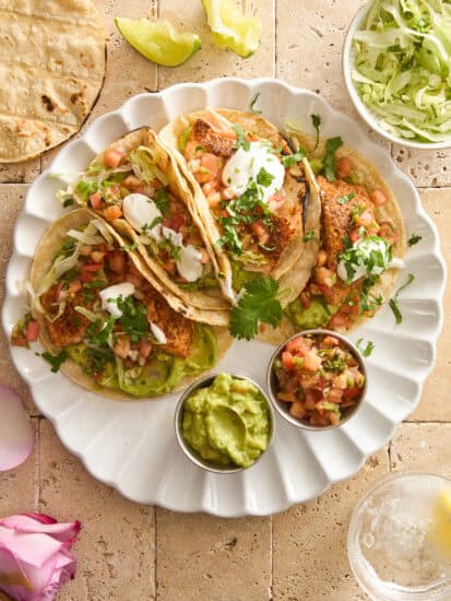 A plate of four salmon tacos with guacamole and pico de gallo.