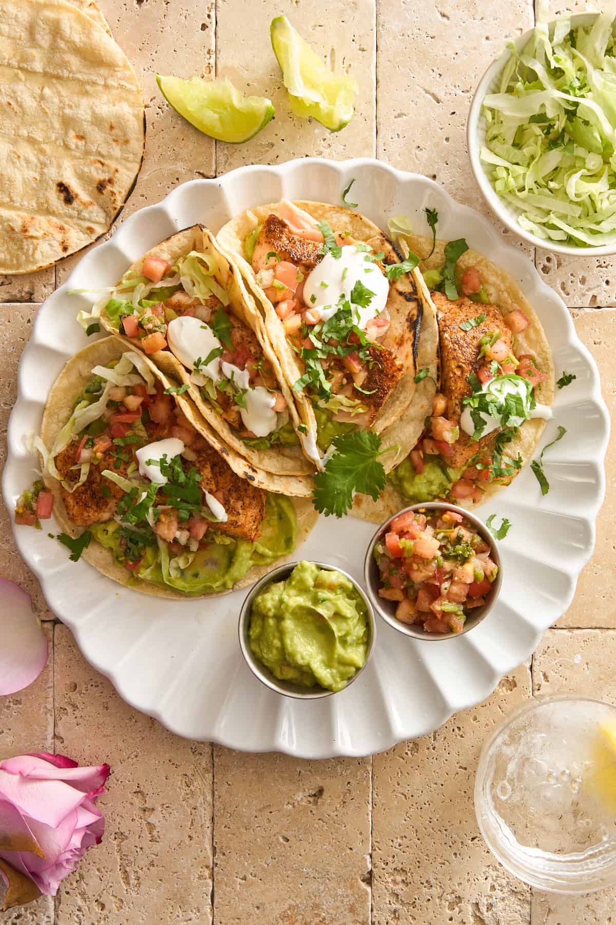 A plate of four salmon tacos with guacamole and pico de gallo. 