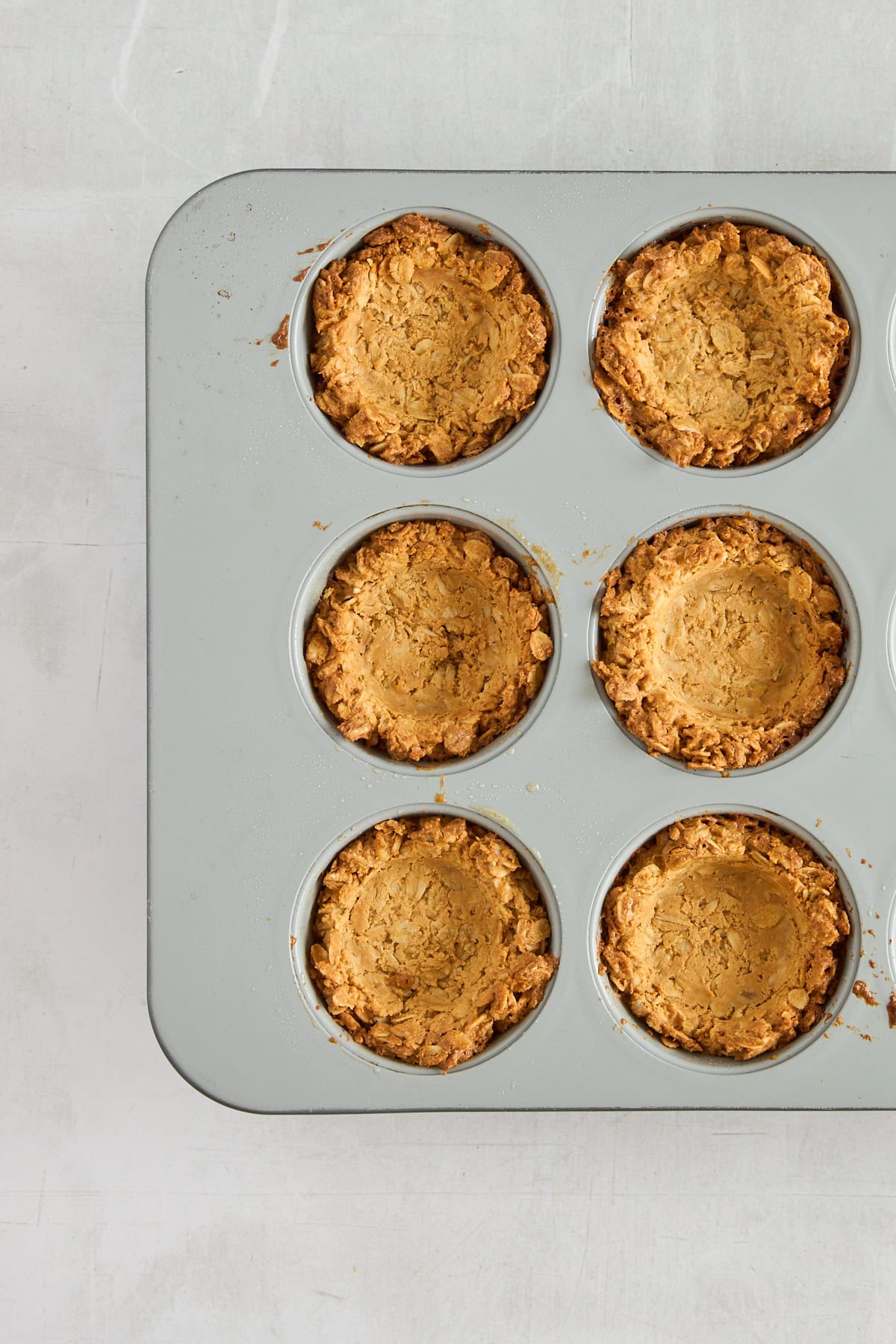 Six baked granola cups in a muffin tin. 