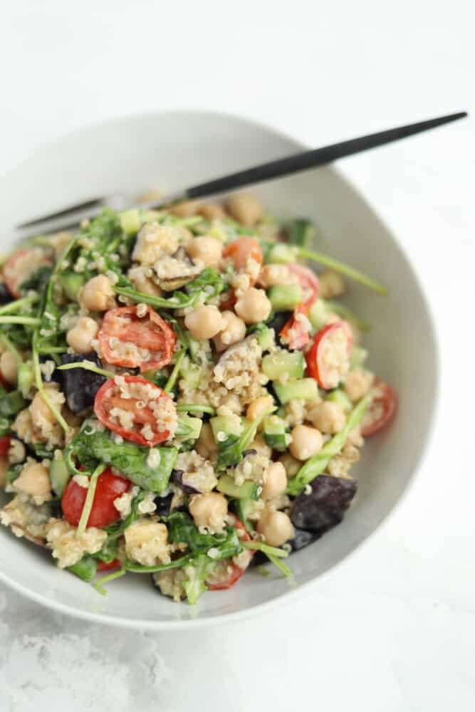 vegan roasted eggplant salad in a white bowl with tahini dressing and quinoa and a chopstick sticking out