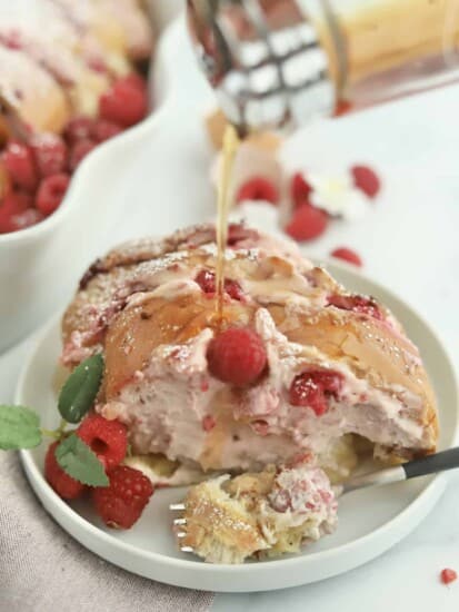 raspberry cheesecake challah french toast on a white plate topped with fresh raspberries