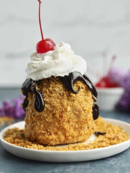 fried ice cream on a plate topped with chocolate sauce, whipped cream, and a cherry.