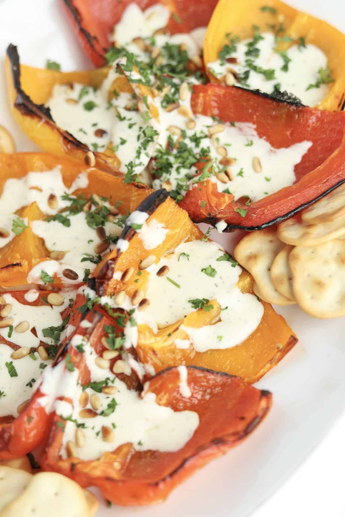 a white serving dish full of quartered roasted peppers and crackers topped with whipped feta, pine nuts, and chopped parsley