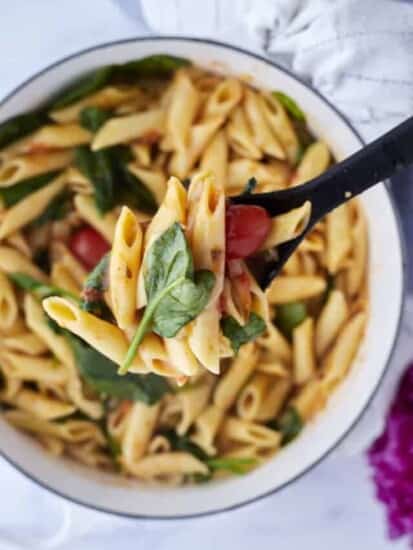 a black serving spoon lifting a scoop of tomato basil one pot pasta out of a white dutch oven full of the recipe