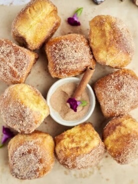 cinnamon bun air fryer french toast buns on a piece of parchment paper with a bowl of cinnamon sugar in the center