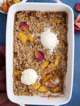 overhead image of a baked peach crisp topped with two scoops of vanilla ice cream with a serving missing out of the bottom righthand corner.